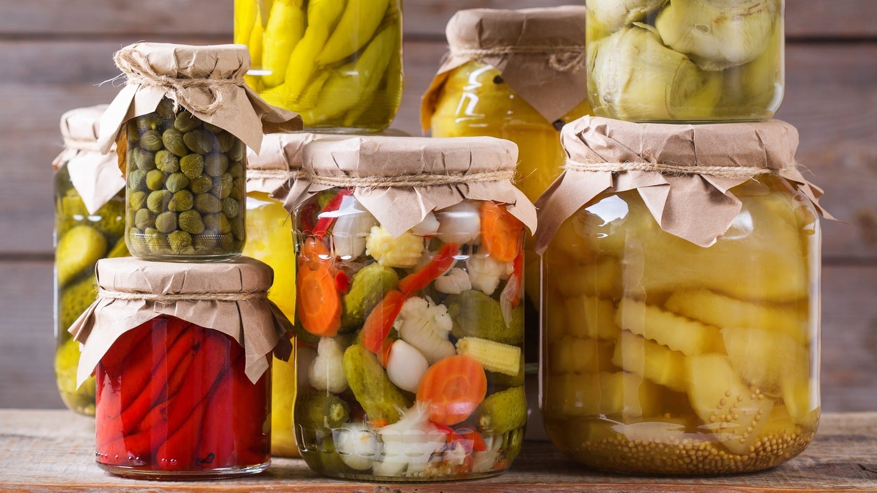 Mixed Pickles, gemischtes eingelegtes Gemüse in einem Einmachglas, umgeben von weiteren Gläsern mit eingemachtem Gemüse.