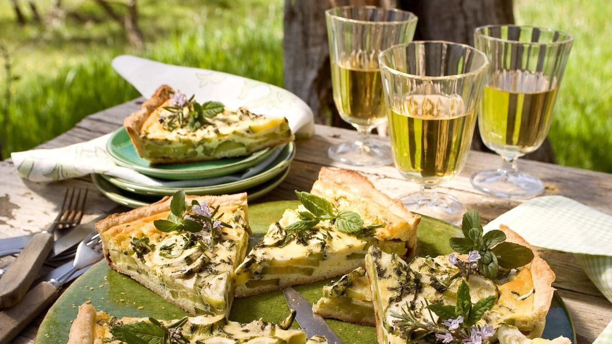 Zucchini-Quiche mit Pfefferminze und Weingläser auf einer Picknickdecke