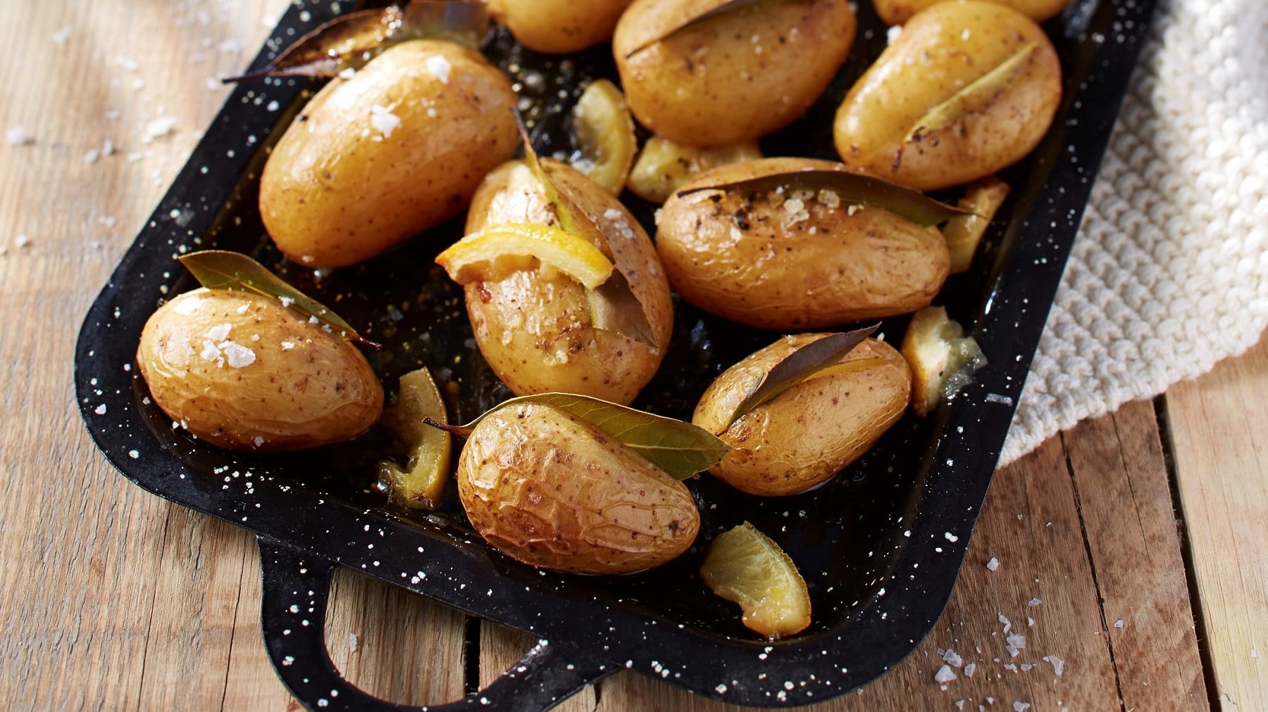 Auf einem Blech liegen Kartoffeln, in denen jeweils ein Lorbeer-Blatt steckt. Drumherum liegen Zitronenscheiben.