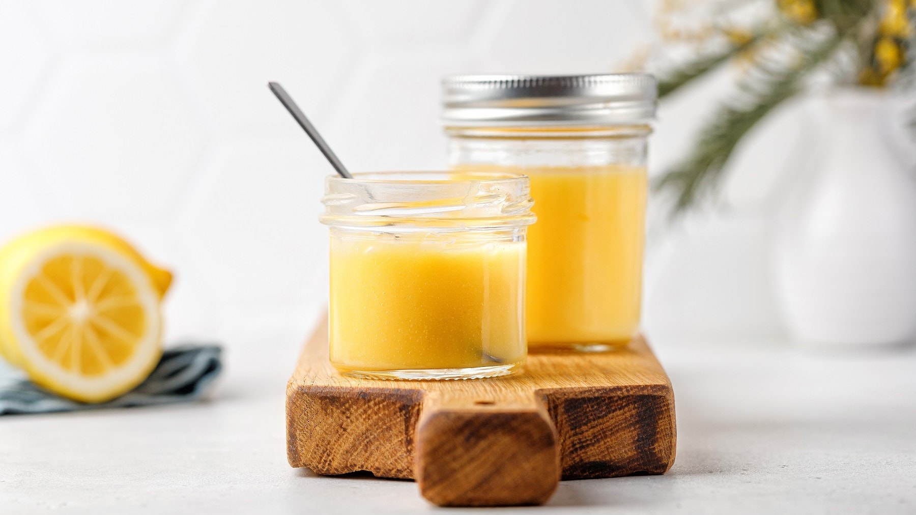 Selbst gemachtes Lemon Curd, abgefüllt in Einweck-Gläser und auf einem Holzbrett vor hellem Hintergrund serviert.