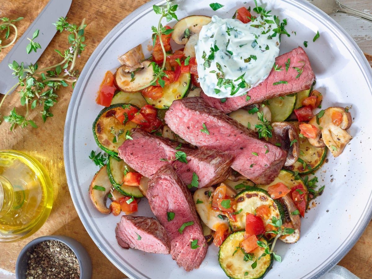 Steakstreifen auf mediterranem Gemüse auf Teller serviert.