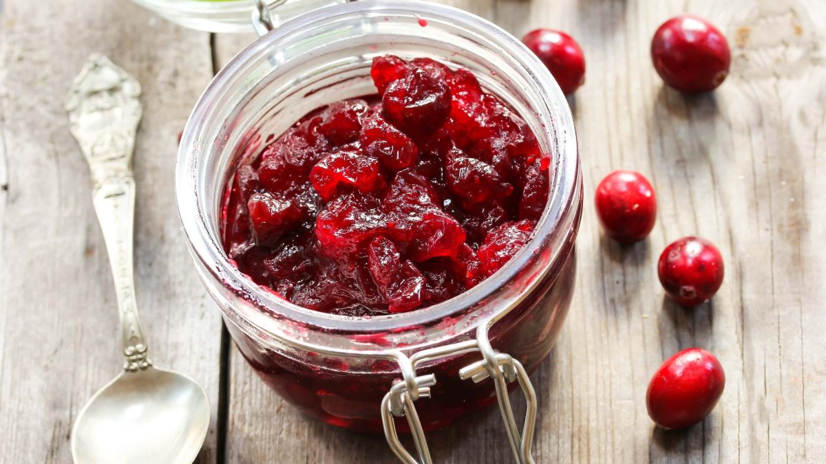 Cranberry-Chutney auf Holztisch mit einzelnen Cranberries und einem silbernen Löffel.