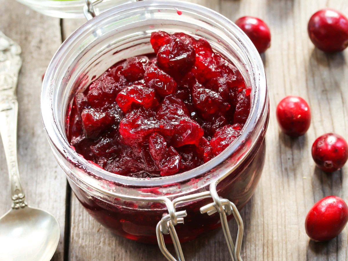 Cranberry-Chutney auf Holztisch mit einzelnen Cranberries und einem silbernen Löffel.