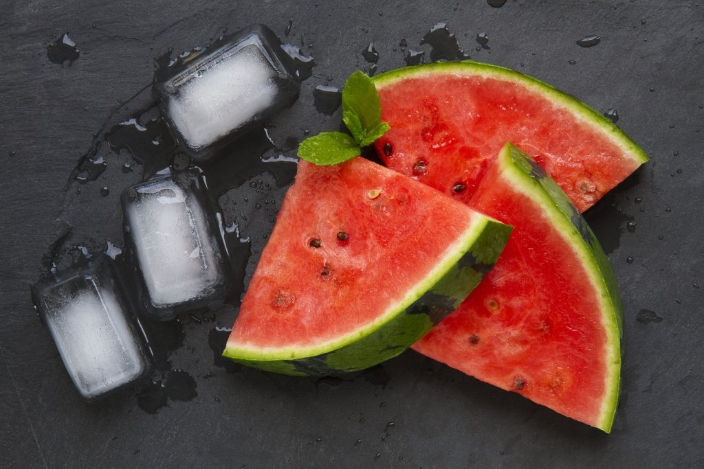 Abnehmen mit Melonen: frisch geschnittene Melonenscheiben mit Eiswürfeln auf dunklem Untergrund