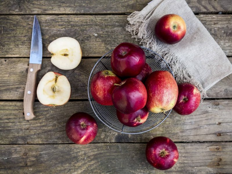 Äpfel mit Messer, Tuch und Obstkorb auf Holz-Untergrund