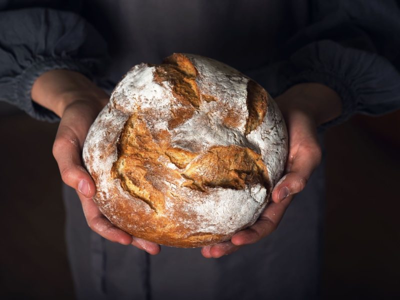 Laib Brot in Händen gehalten, schwarzer Hintergrund
