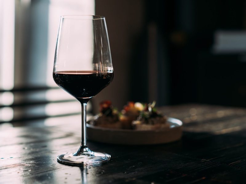 Ein Glas Rotwein auf einem dunklen Holztisch vor einem dunklen Hintergrund.