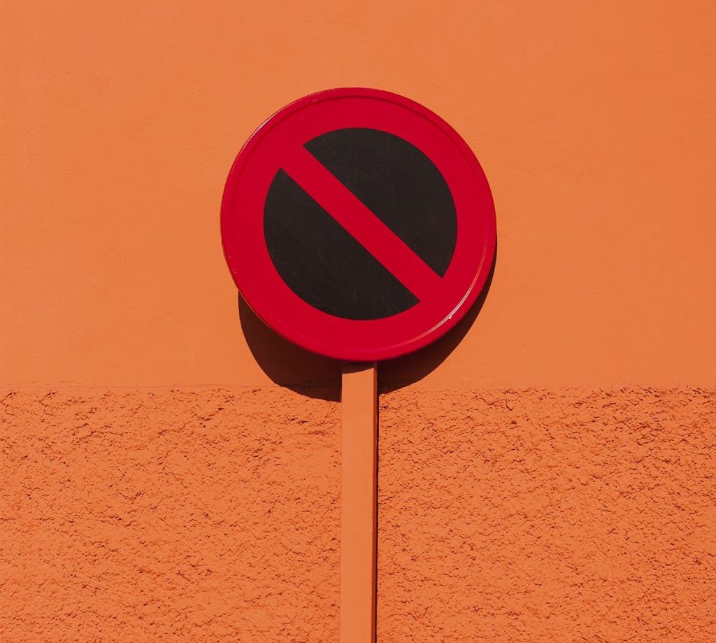 Rot-Schwarzes Verbotsschild mit orangenem Griff vor einer orangenen Wand