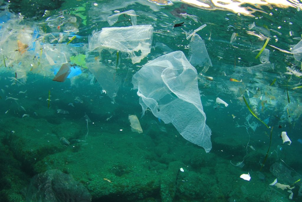Verschiedener Plastikmüll schwimmt im Meer unter der Wasseroberfläche. Darunter verschiedene Verpackungen und Plastiktüten. Unterhalb vom Müll befindet sich der Meeresboden.