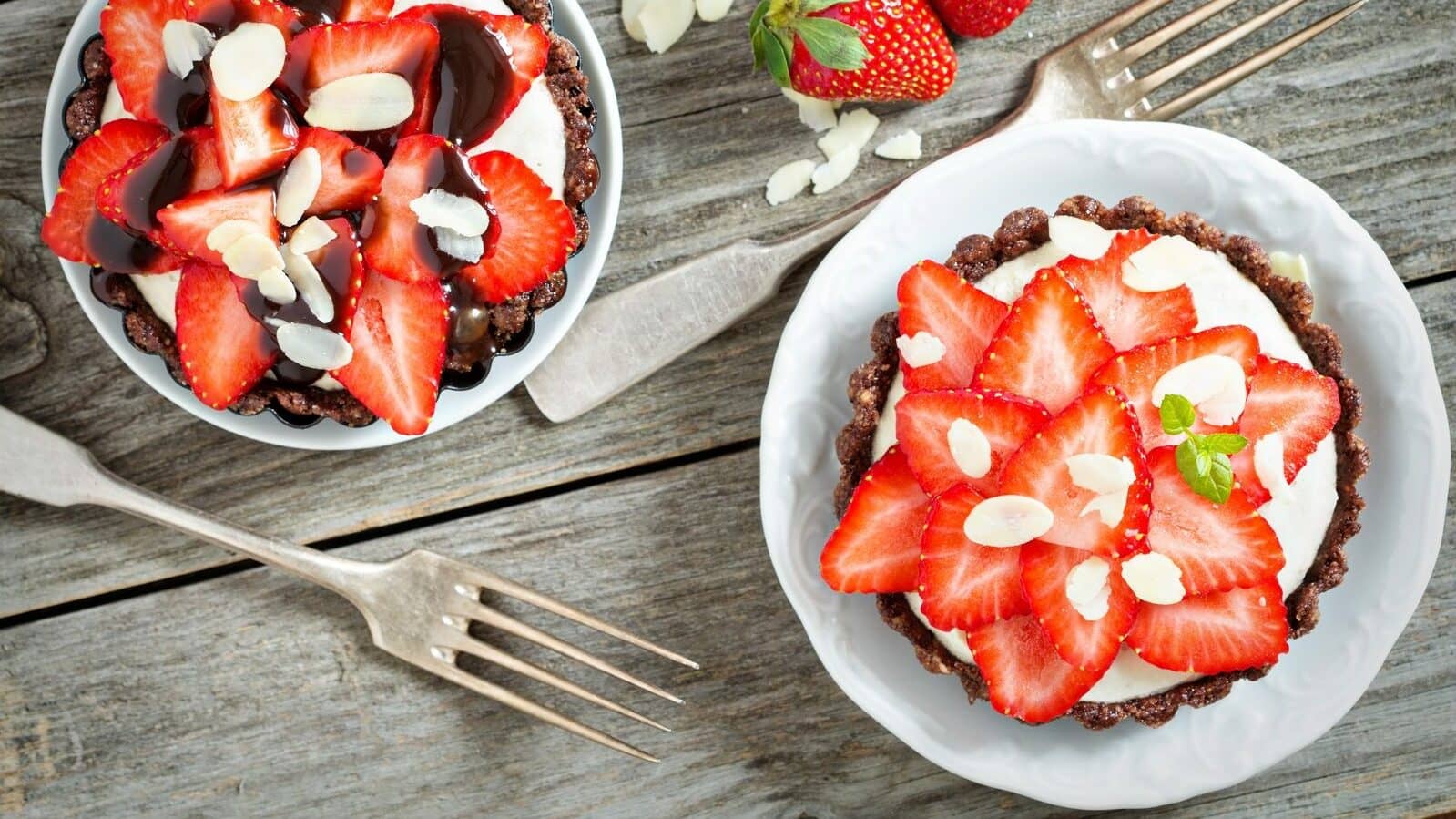 Zwei Schokoladen tartelettes mit Erdbeersahne und Erdbeer-Verziehrung von Oben auf einem Holztisch