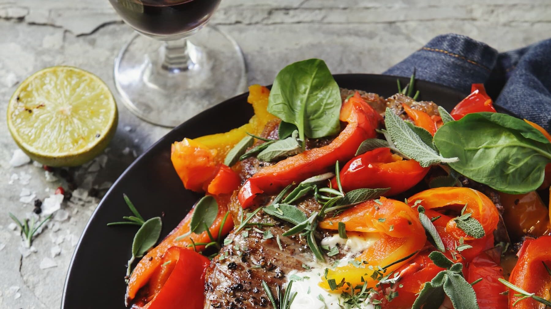 Schnelles Steak mit Paprika-Salat auf schwarzem Teller mit Steinhintergrund und einem Glas