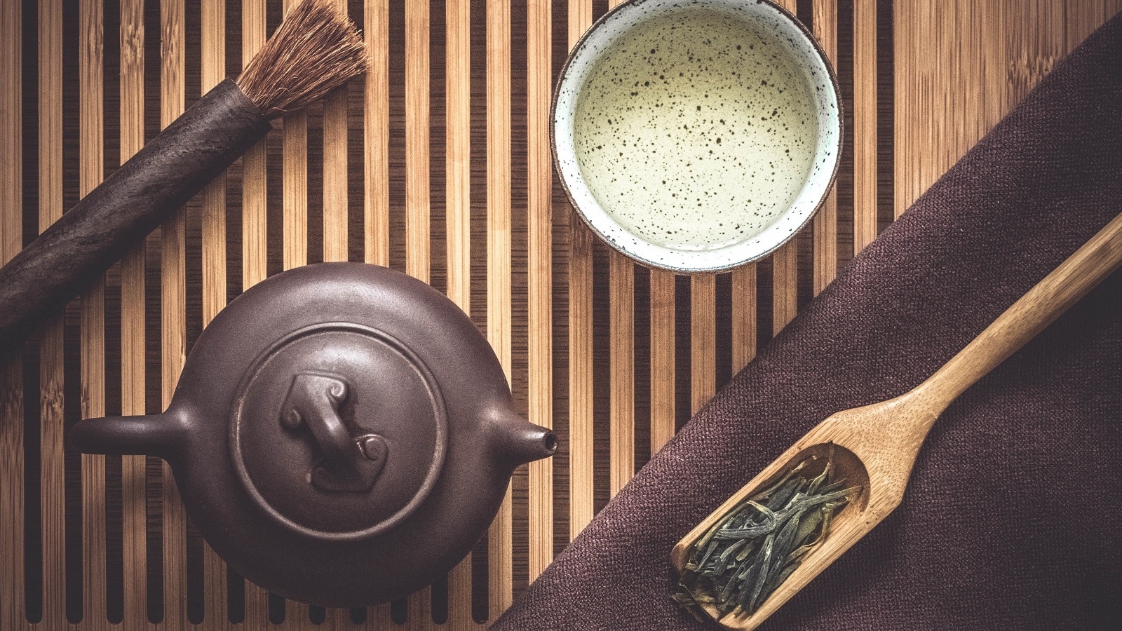 Weißer Tee, Teezeremonie: Braune Teekanne neben einer Tasse mit Weiß Tee, einem Bambuslöffel mit getrockneten Teeblättern und einem Pinsel auf hölzernem Hintergrund, von Oben.