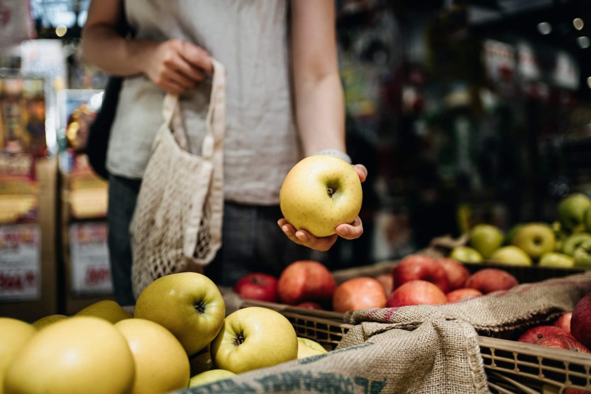 deutscher Fruchtpreis 2021: Eine Frau im close-up an einem Obststand mit einem Apfel in der Hand.