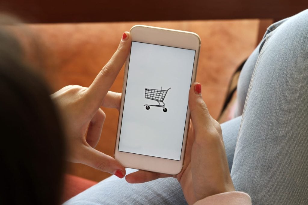 Lebensmittellieferanten online bestellen: Eine Frau hält ein Handy in der Hand, auf dem eine Bestellapp geöffnet wird.