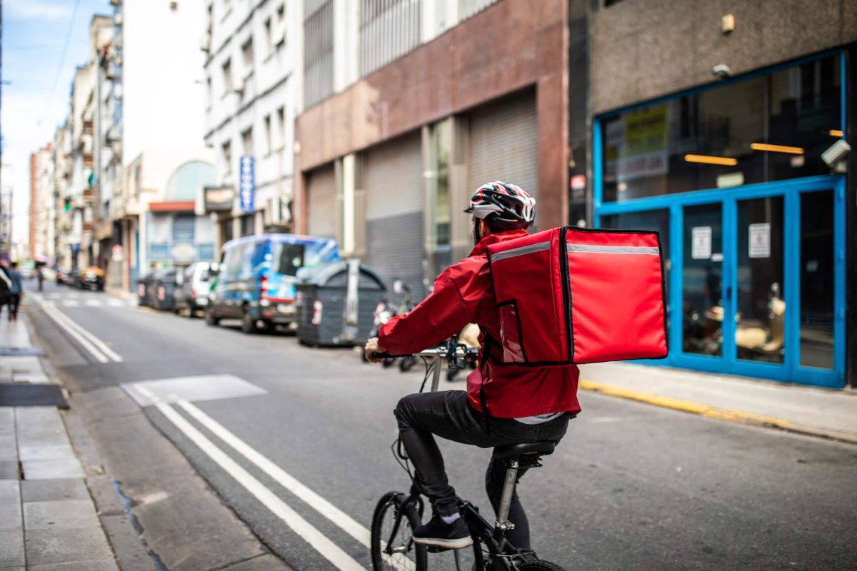 Lebensmittellieferanten im Vergleich: Ein Fahrrad-Kurier mit einem Lieferrucksack unterwegs auf einer Straße