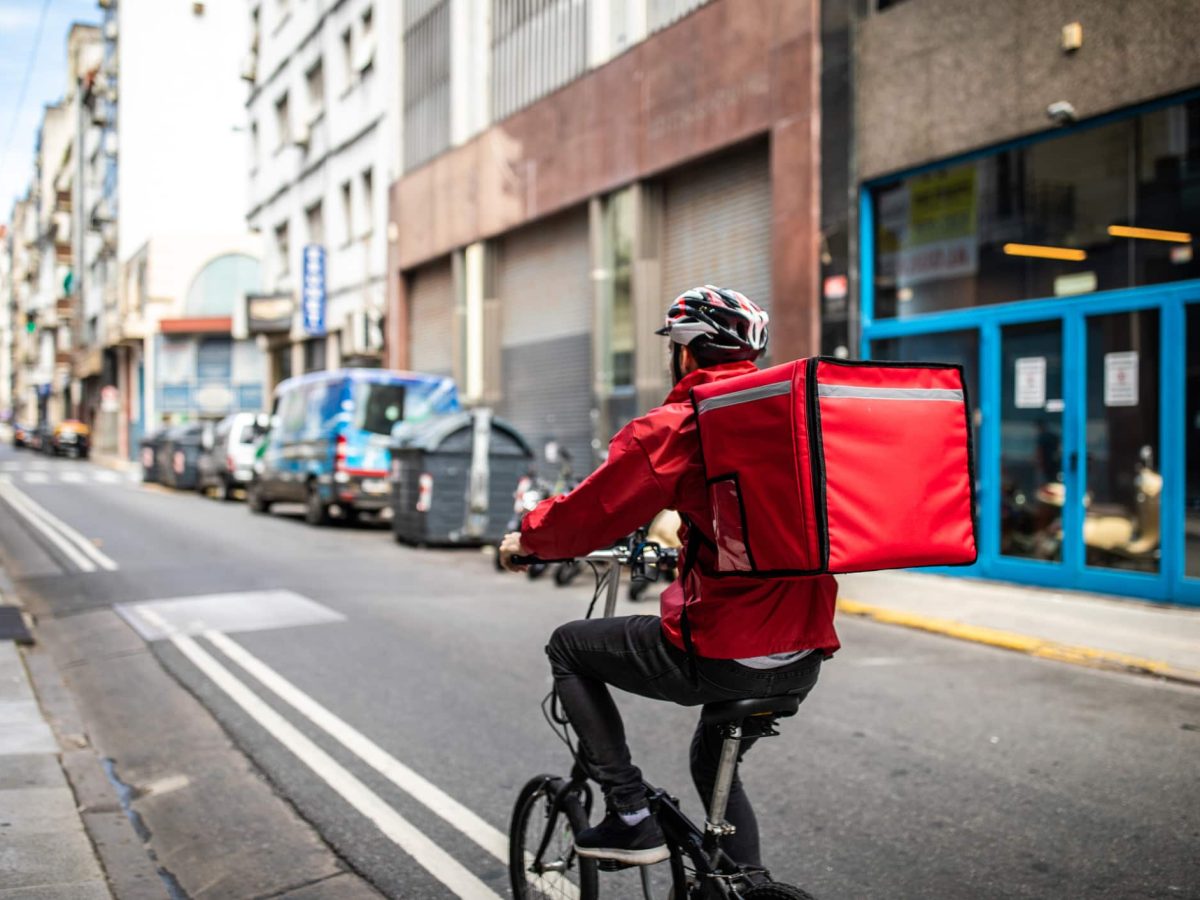 Lebensmittellieferanten im Vergleich: Ein Fahrrad-Kurier mit einem Lieferrucksack unterwegs auf einer Straße