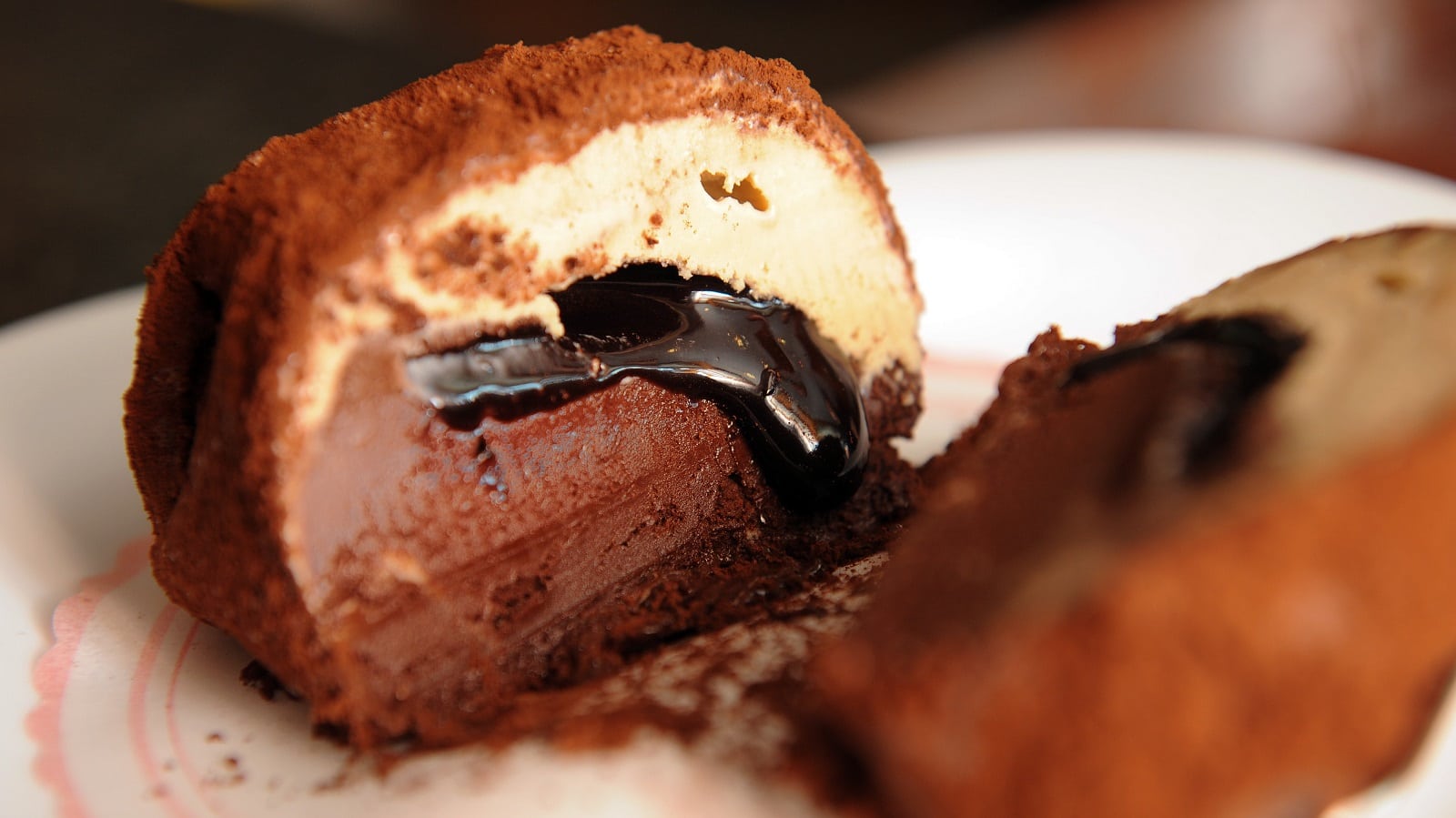 Ein aufgeschnittener Tartufo di Pizzo der einen Blick auf die Schokoladeneis, Haselnusseis Schichten mit der Schokoladensoße-Füllung freigibt.