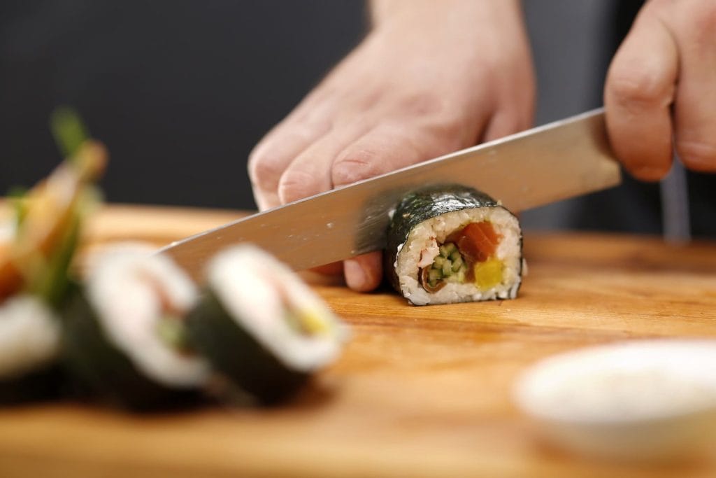 Eine Rolle Sushi wird mit einem scharfen Messern in mehrere Stückchen geschnitten.