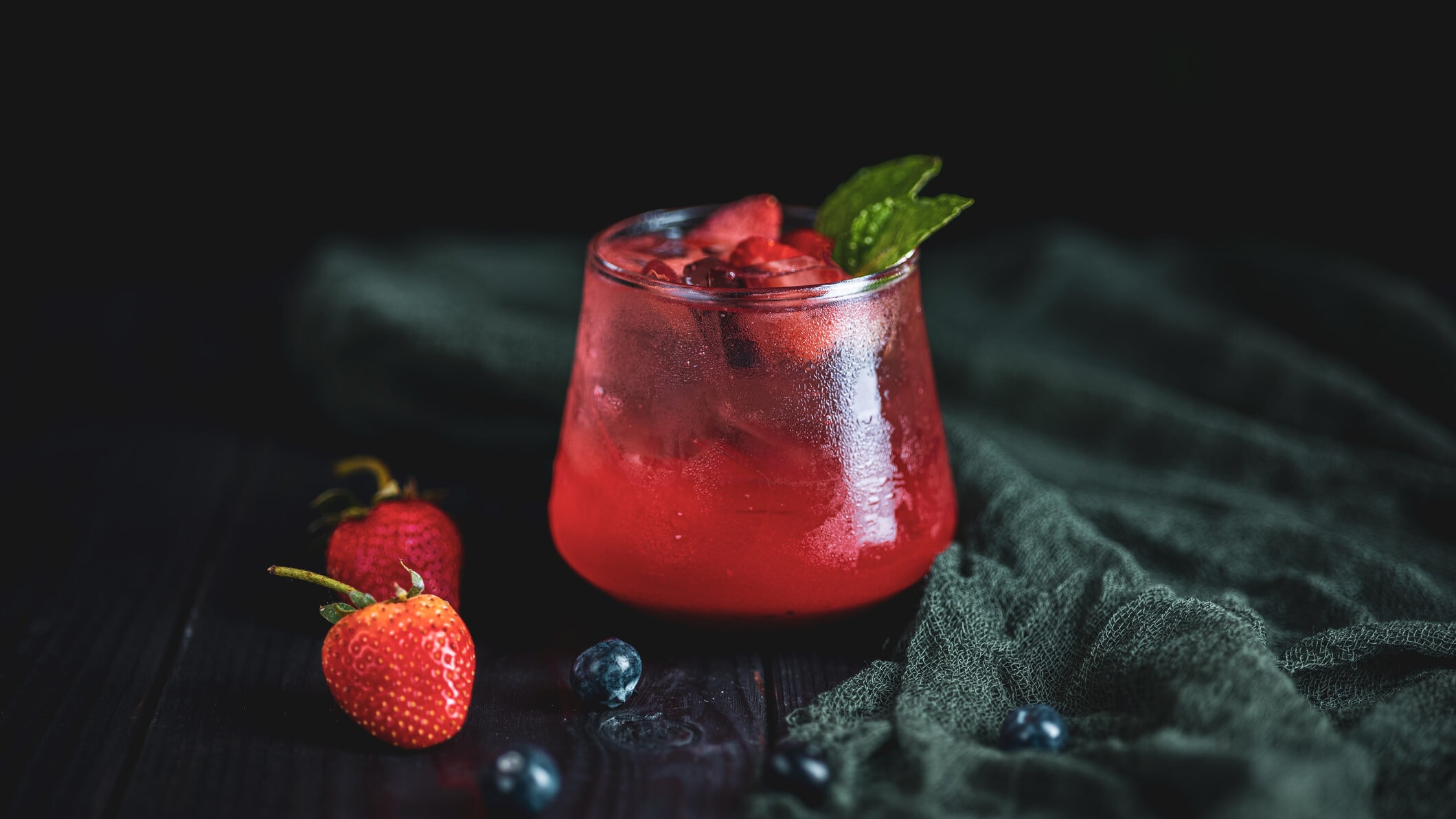 Ein Glas mit rotem Berlin Berry Cocktail, dekoriert mit frischen Beeren, vor einem dunklen Hintergrund.