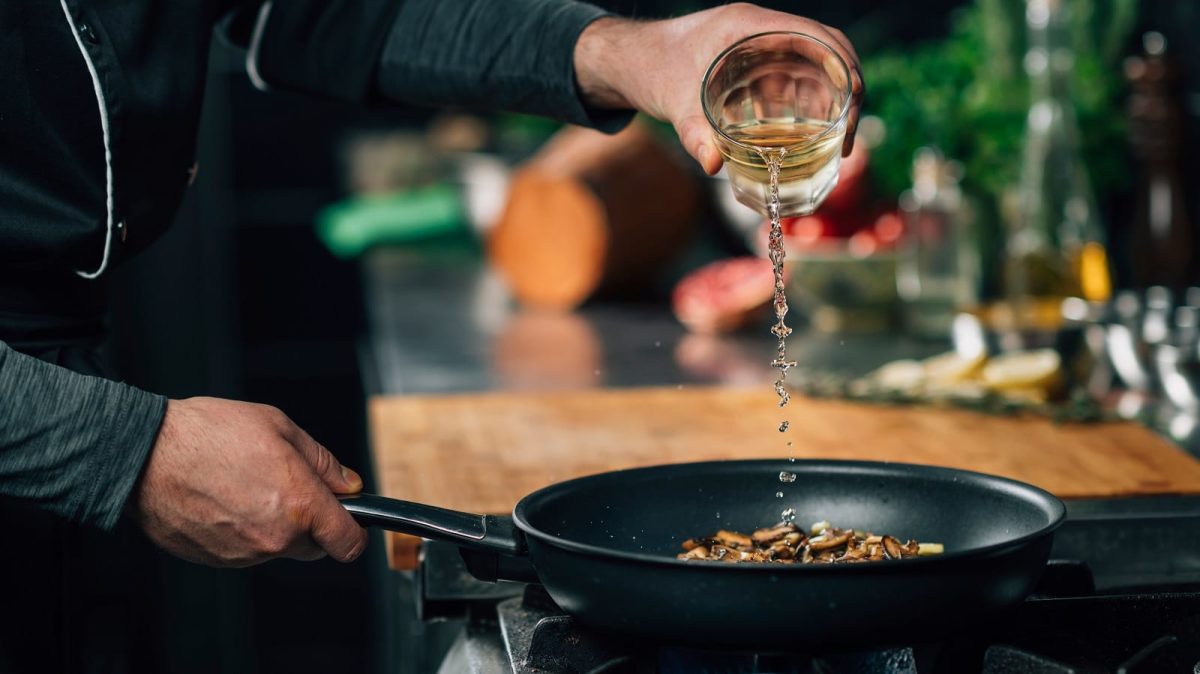 Ablöschen in der Praxis: Ein Koch gießt Weißwein in eine Pfanne mit Gemüse.
