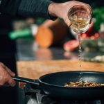 Ablöschen in der Praxis: Ein Koch gießt Weißwein in eine Pfanne mit Gemüse.