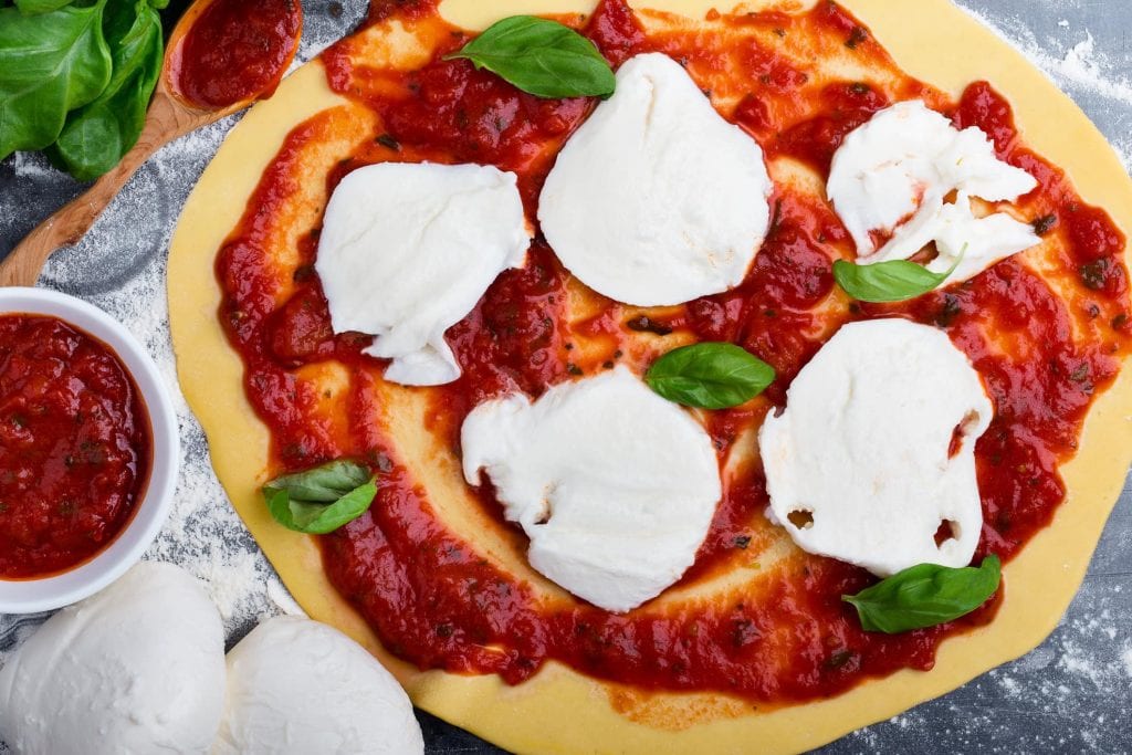 Pizza-Teig mit Tomatensoße, Mozzarella und Basilikum