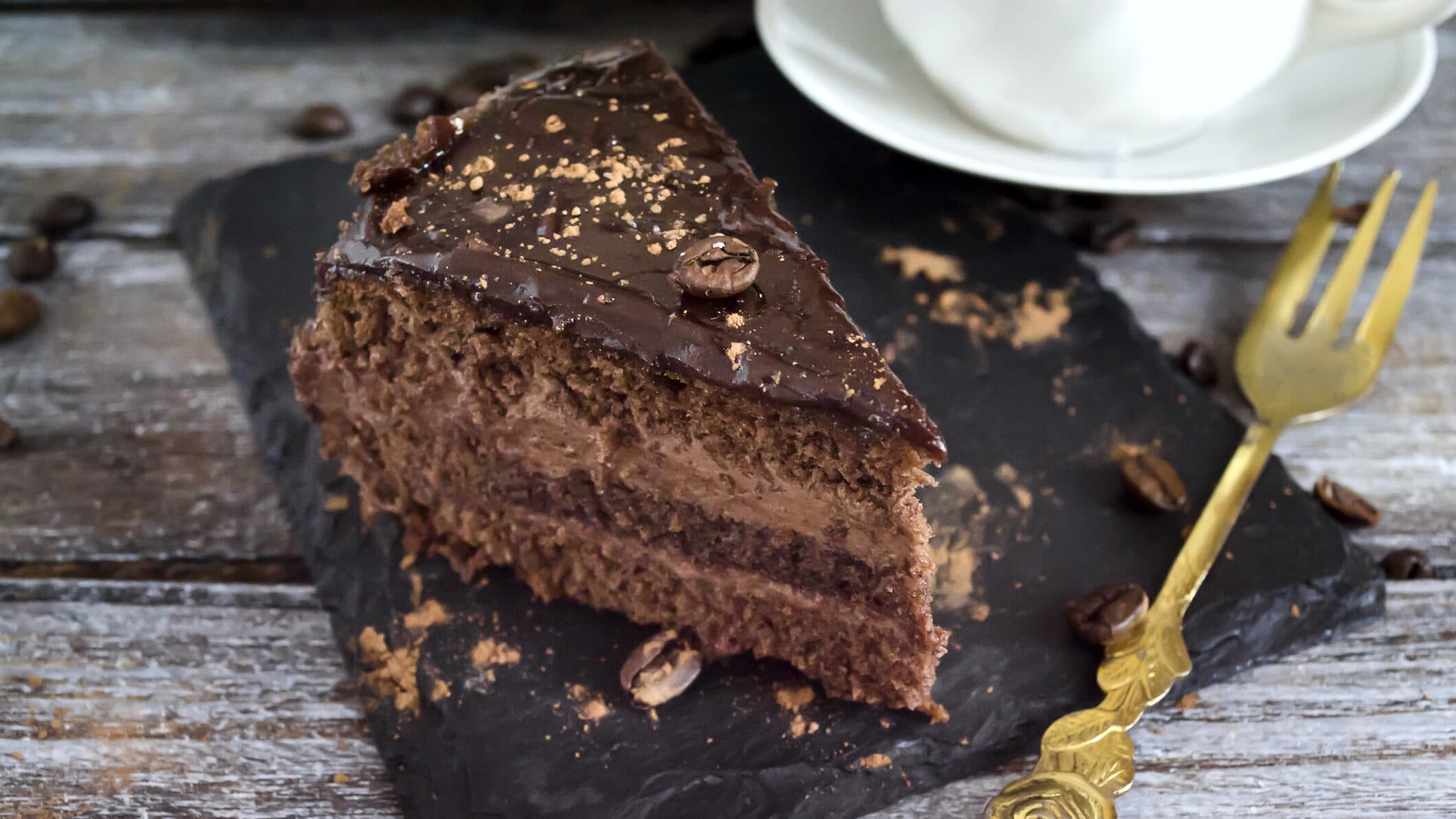 Ein Stück Mousse-au-Chocolat-Torte auf einer Schieferplatte, daneben liegt eine goldene Kuchengabel.