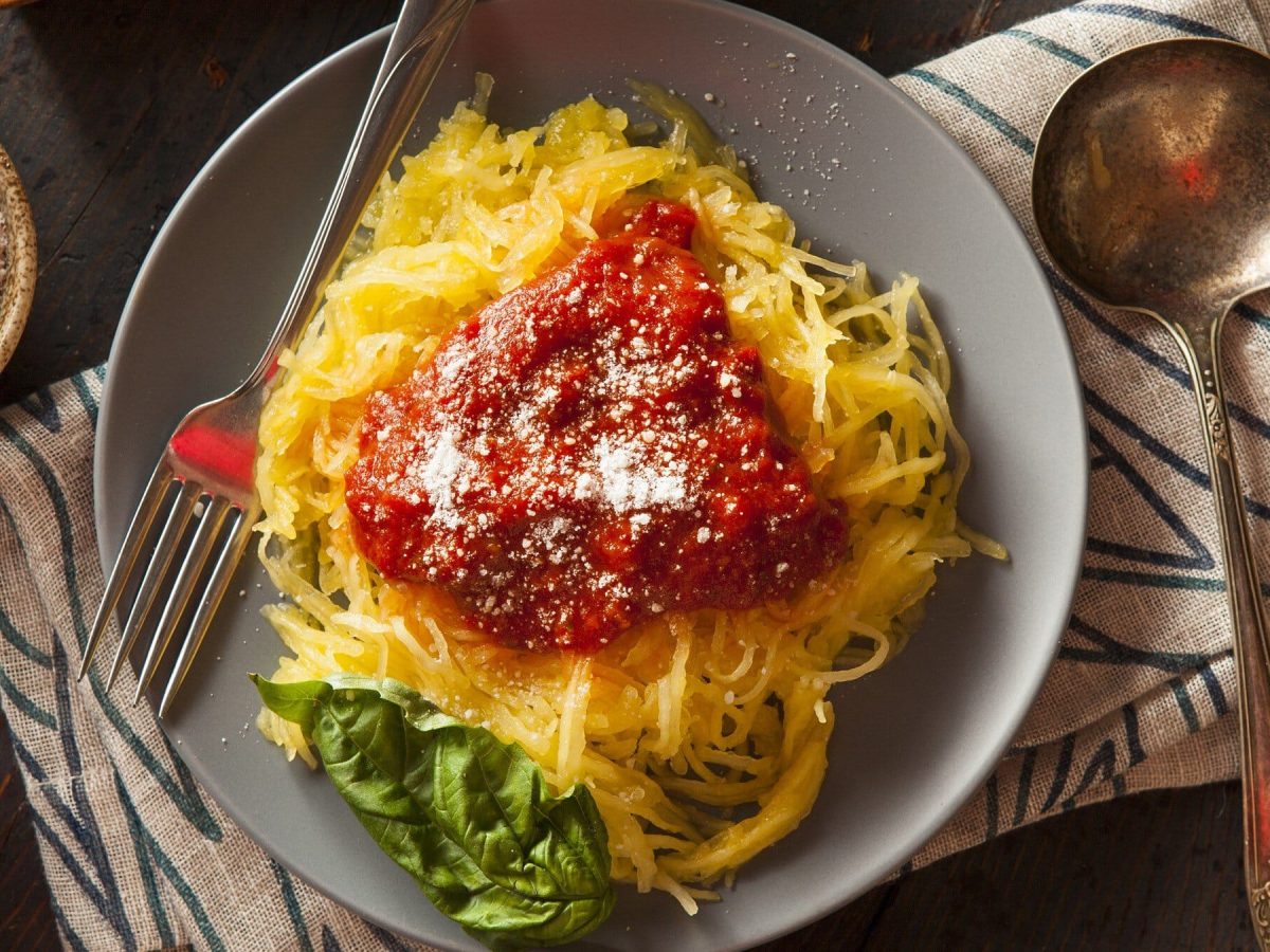 Teller mit Spaghettikürbis, Tomatensoße, geriebenem Käse und einem Basilikum-Blatt.