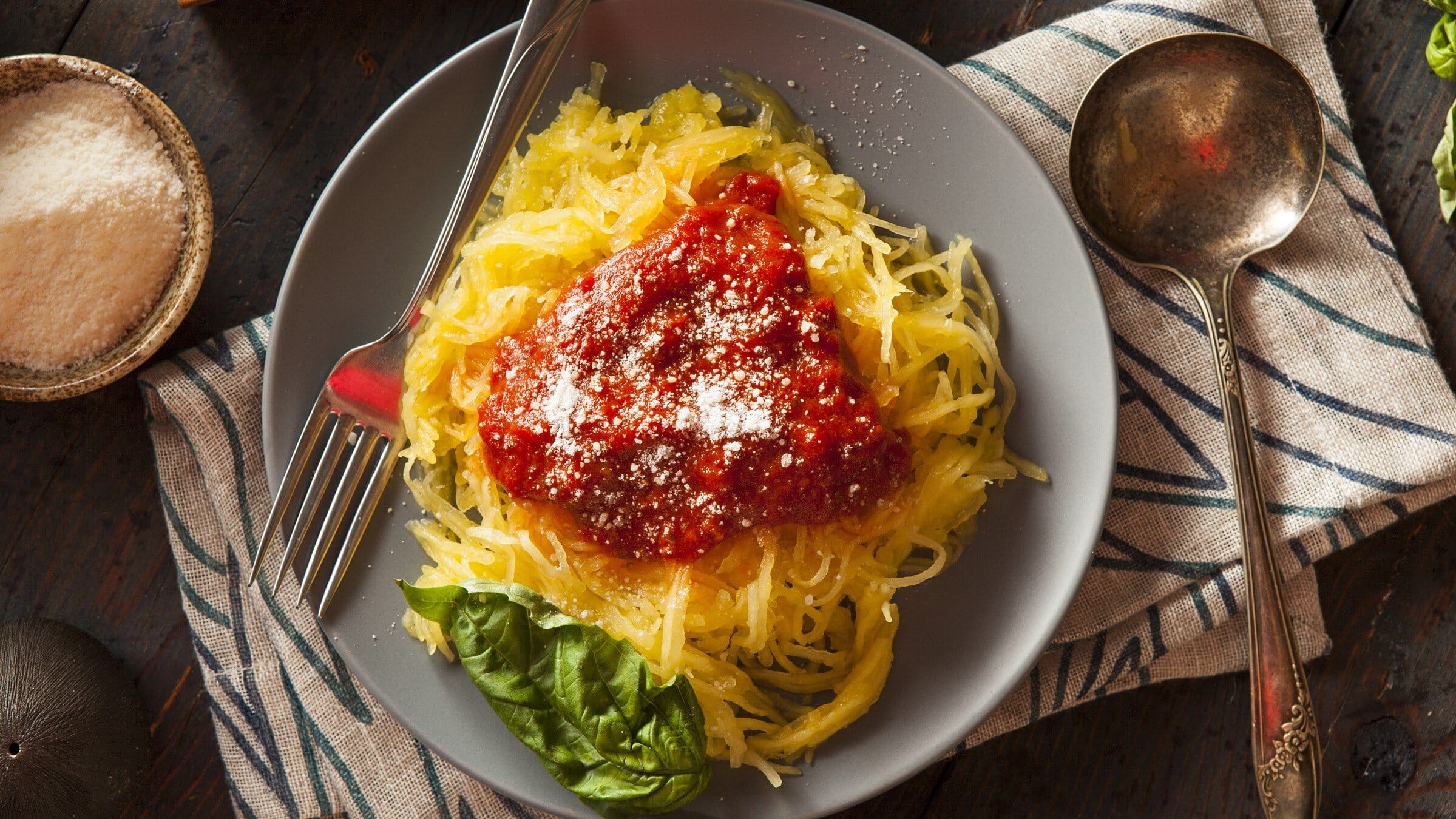 Teller mit Spaghettikürbis, Tomatensoße, geriebenem Käse und einem Basilikum-Blatt.