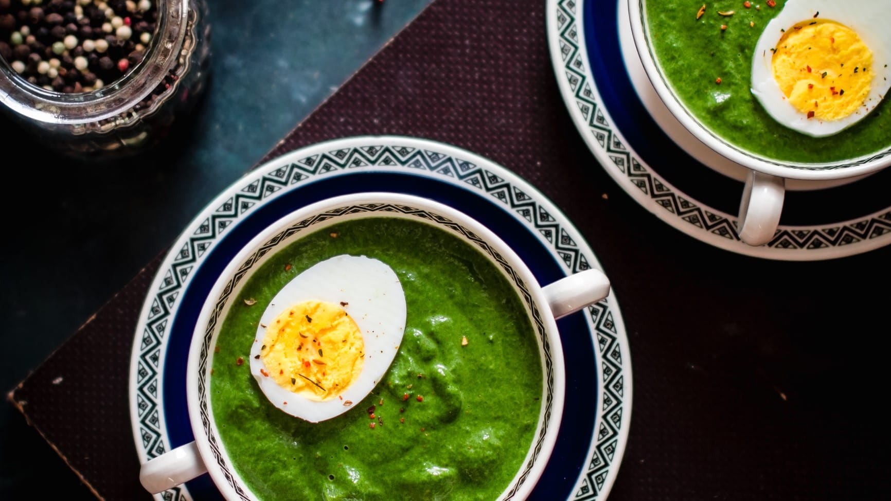 Zwei kleine Suppenschüsseln mit Grünkohl-Rahmsuppe mit einem halben Ei in der Draufsicht.