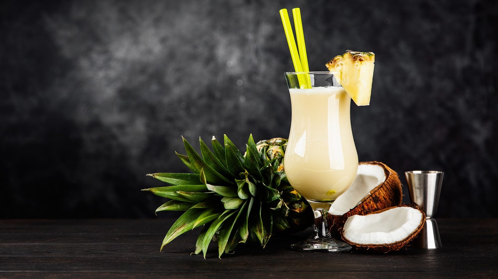 Die Low Carb-Pina Colada stilecht im Glas angerichtet, mit Ananas am Rand verziert und die Kokosnuss als Deko im Hintergrund.