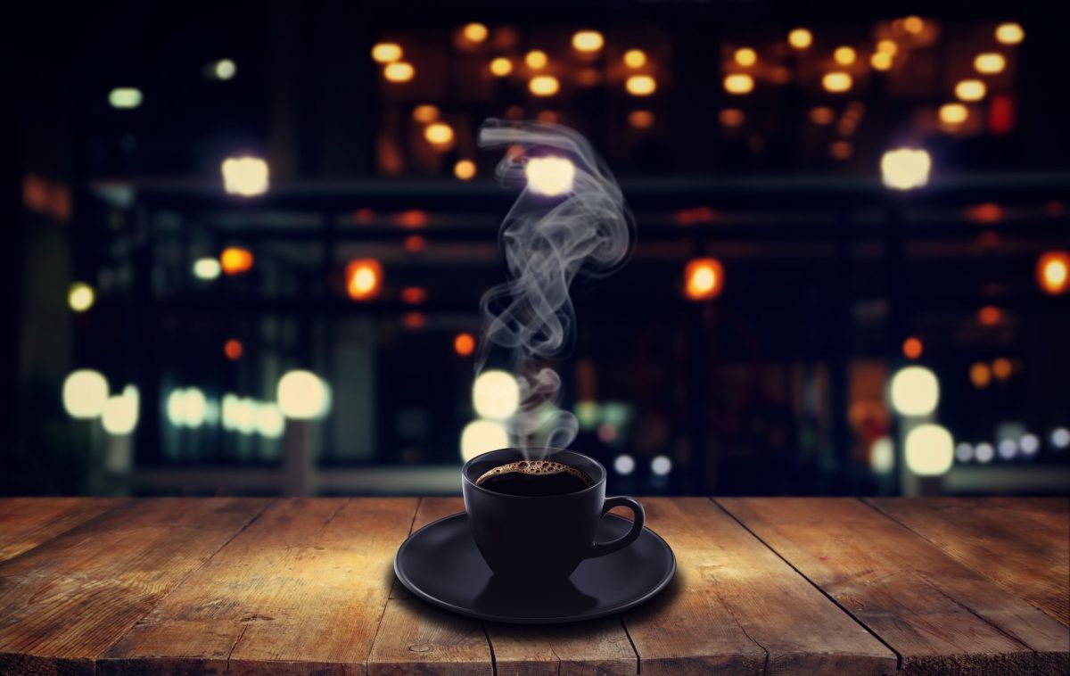 Tasse dampfender Kaffee steht auf dem Tresen einer dunklen Bar