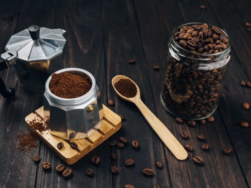 Kaffeebohnen, gemahlener Kaffee und ein Espressokocher auf dunklem Holz