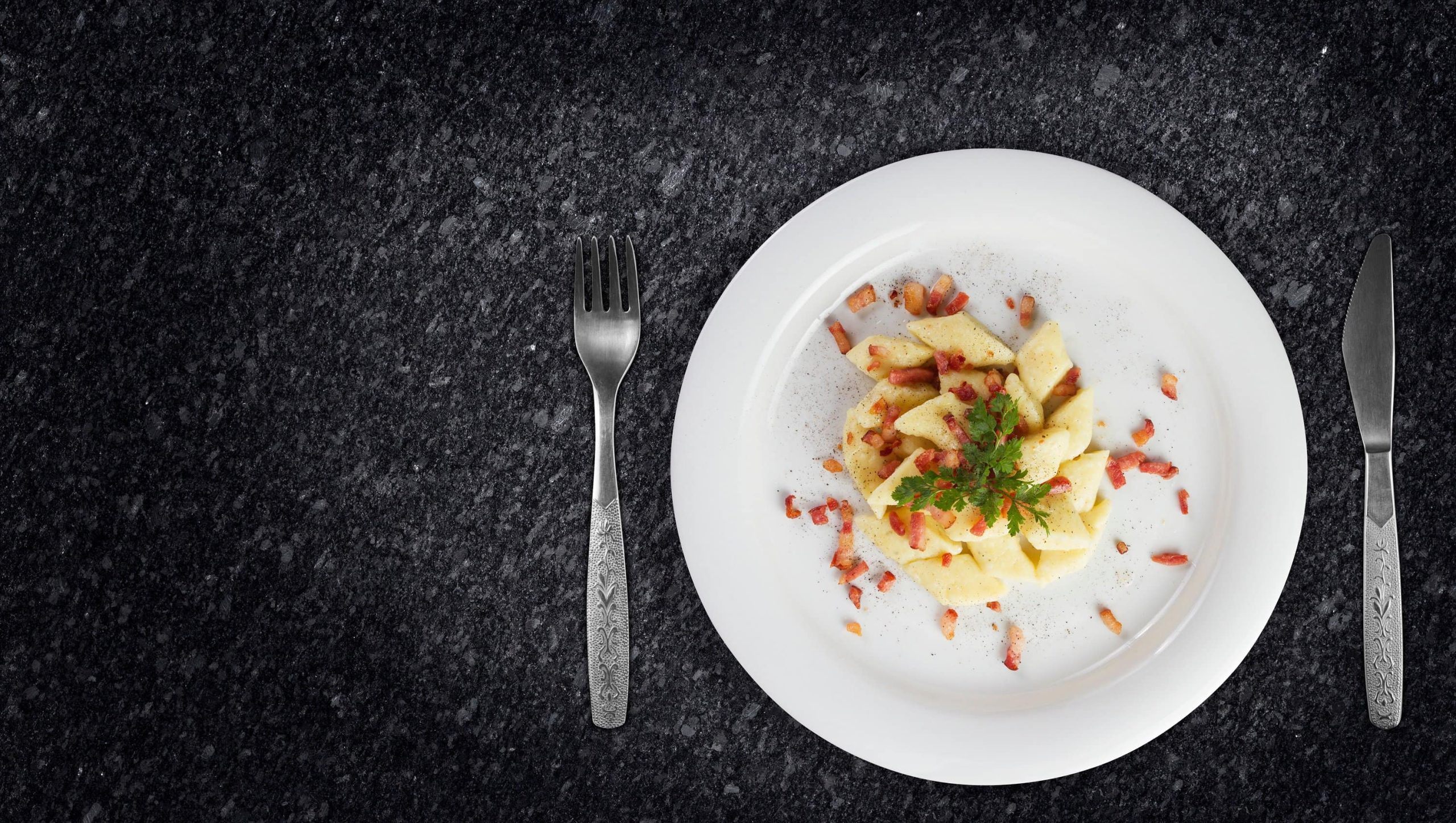 Polnische Kartoffelklöße Kopytka auf weißem Teller, serviert auf dunkler Arbeitsplatte.