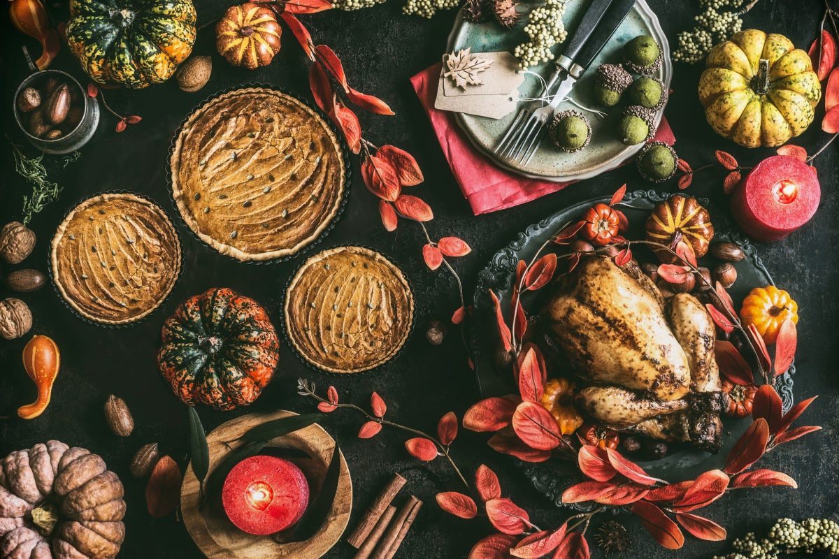 Ein Thanksgiving-Dinnertisch in der Draufsicht, darauf ein Truthahn, Kuchen, Aufläufe und herbstliche Deko.