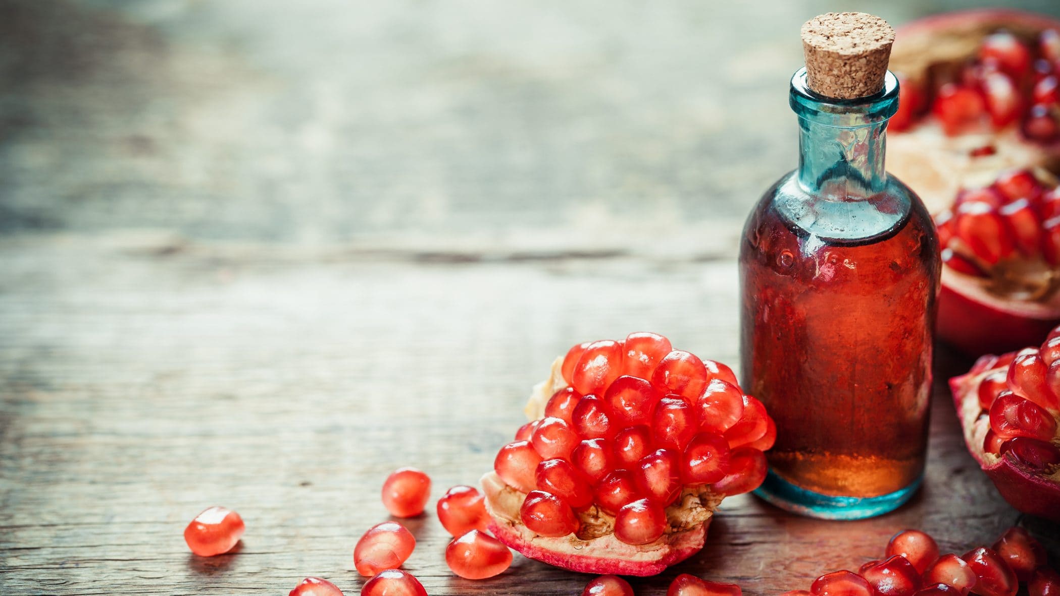 In einer Glasflasche ist eine rote Flüssigkeit. Es handelt sich um Granatapfel-Sirup. Daneben liegen Granatapfelkerne.
