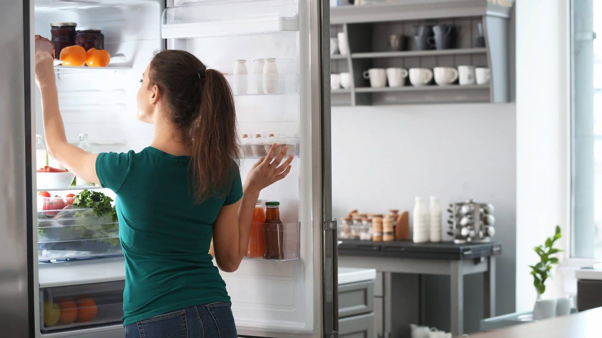 Wie lange ist gekochtes Essen im Kühlschrank haltbar? Frau am Kühlschrank mit Lebensmitteln und Gerichten
