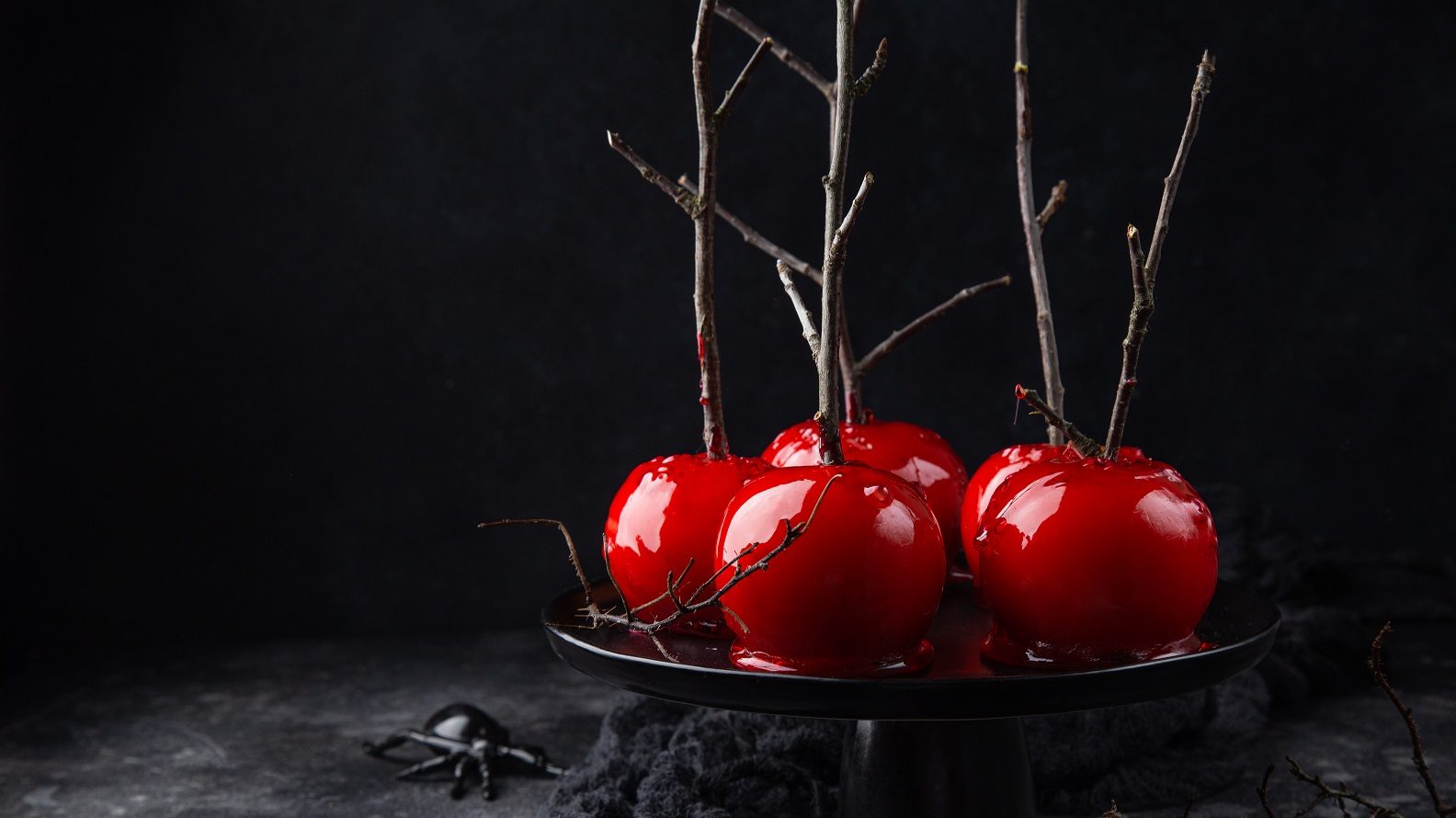 Unsere kandierten Äpfel liegen leicht mystisch angerichtet auf einem schwarzen Teller vor einem schwarzen Hintergrund.