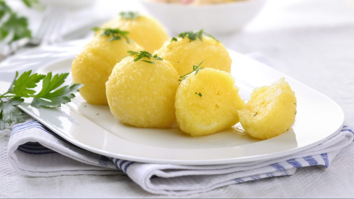 Auf einem weißen Teller liegen sechs Kartoffelknödel