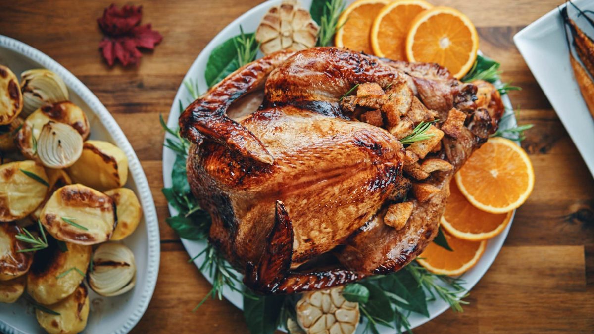In der Draufsicht sieht man einen Thanksgiving-Truthahn auf einem Teller, dekoriert mit Orangenscheiben und Kräutern. Drumherum sieht man einige Beilagen.