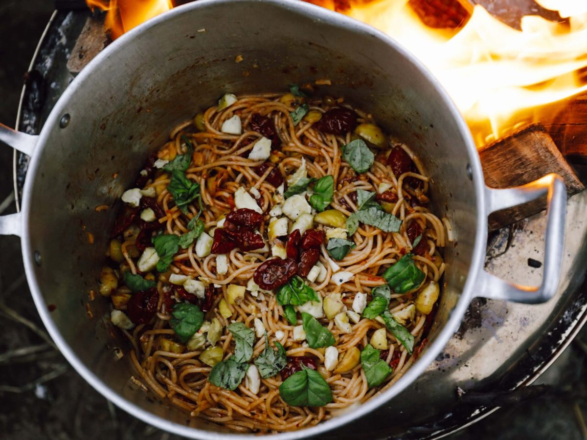 Ein Topf auf einer Feuerschale, darin Maronen-Spaghetti mit getrockneten Tomaten und Basilikum. Das Rezept stammt aus dem Kochbuch "Vegan im Van".