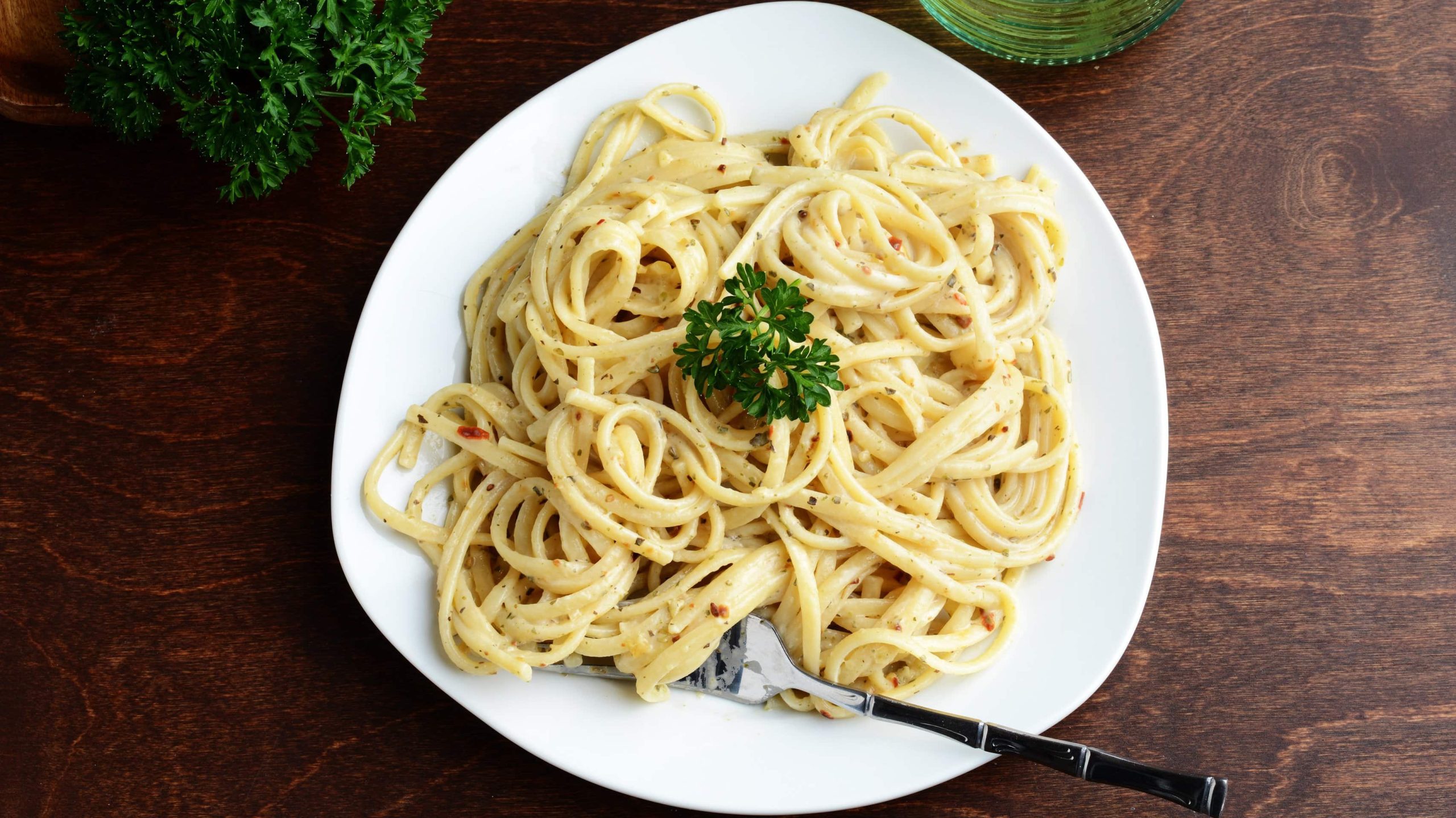 Auf einem Holztisch steht ein Teller in der Draufsicht, darauf vegane Spaghetti Carbonara mit Petersilie dekoriert.