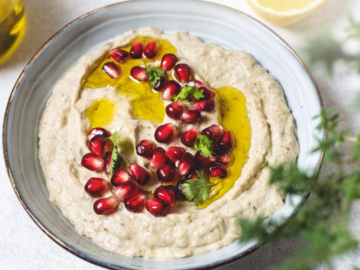 Unser Hummus-Auberginen-Dip sieht mit Granatapfelkernen, Koriander und Olivenöl angerichtet einfach nur köstlich aus.
