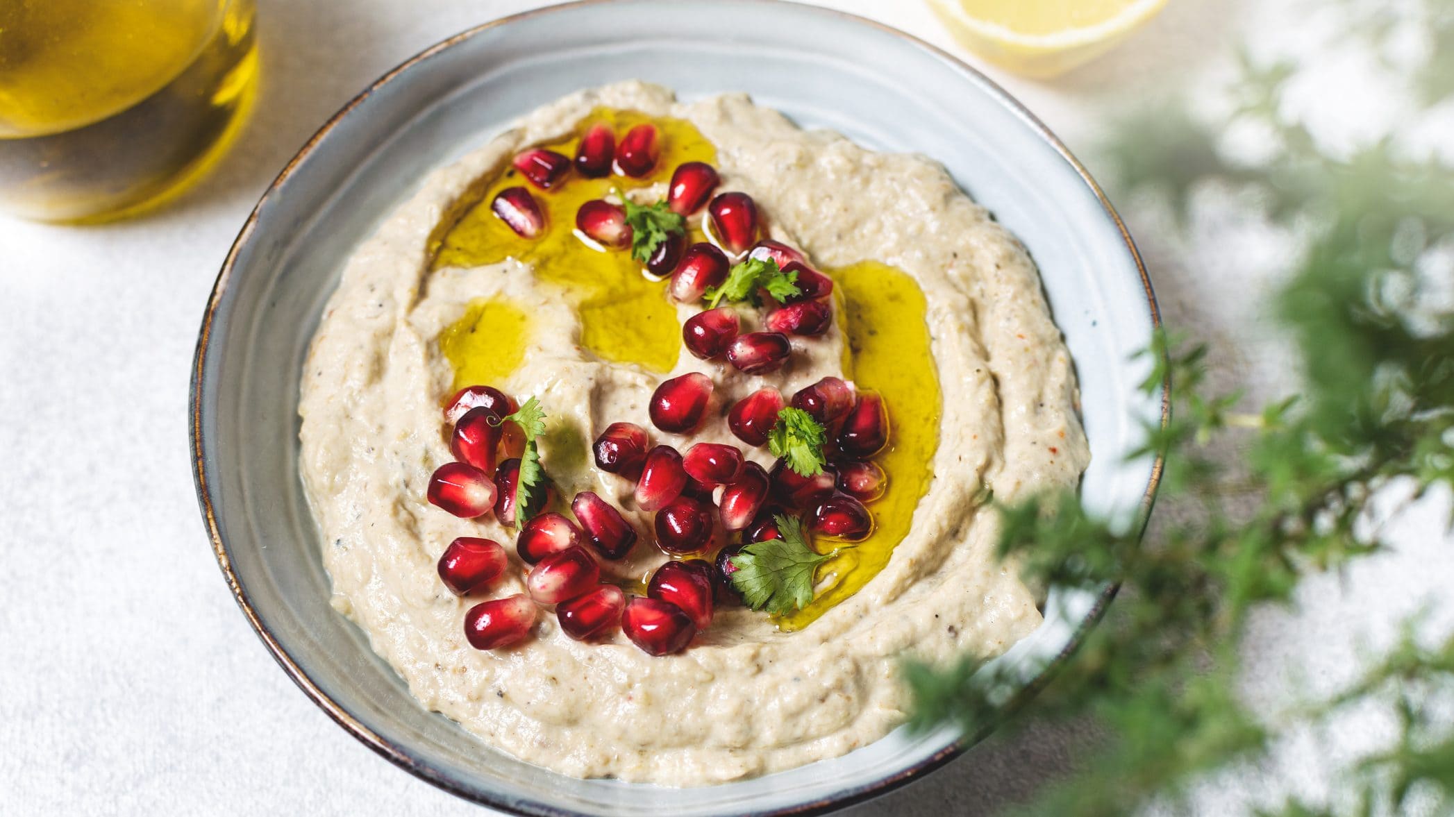 Unser Hummus-Auberginen-Dip sieht mit Granatapfelkernen, Koriander und Olivenöl angerichtet einfach nur köstlich aus.