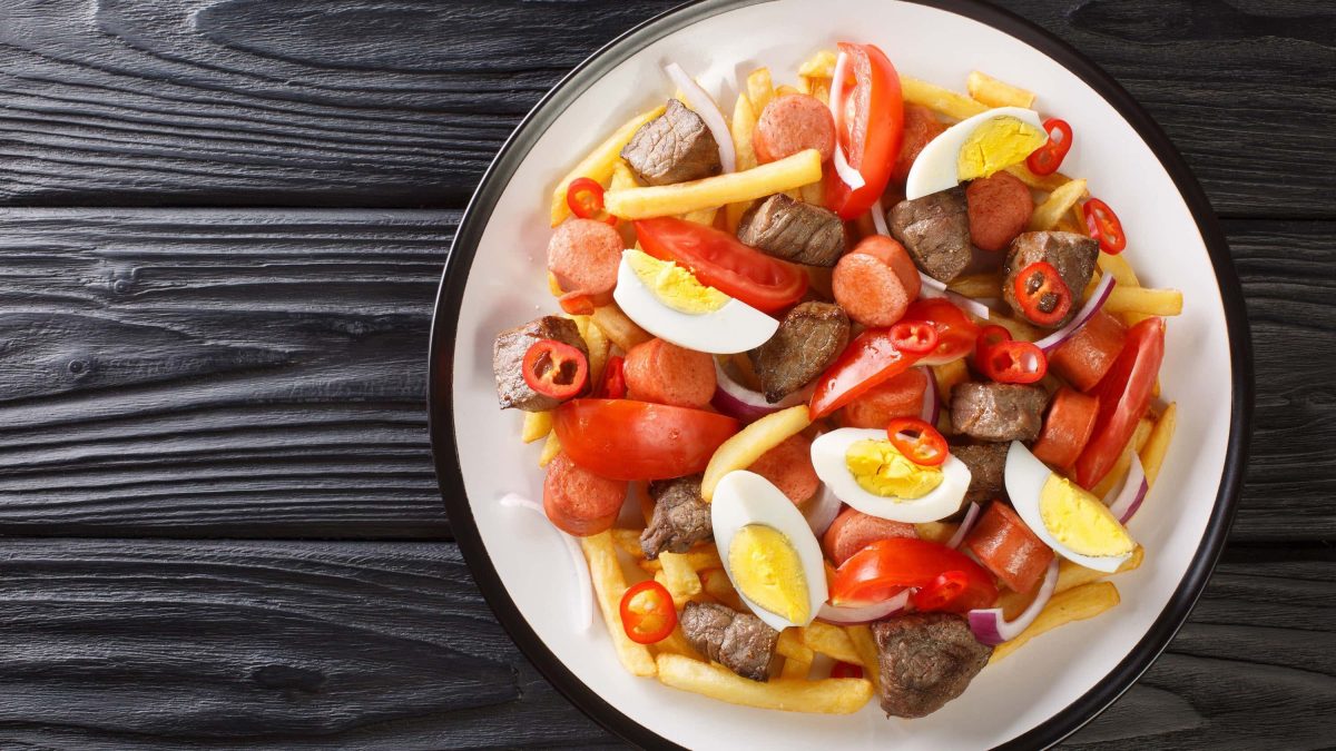 Pique Macho: Bolivianisches Gericht auf einem Teller mit Tomaten, Rindfleischstücken, Chorizo, Pommes, gekochtem Ei, Tomaten, Chili und Soße