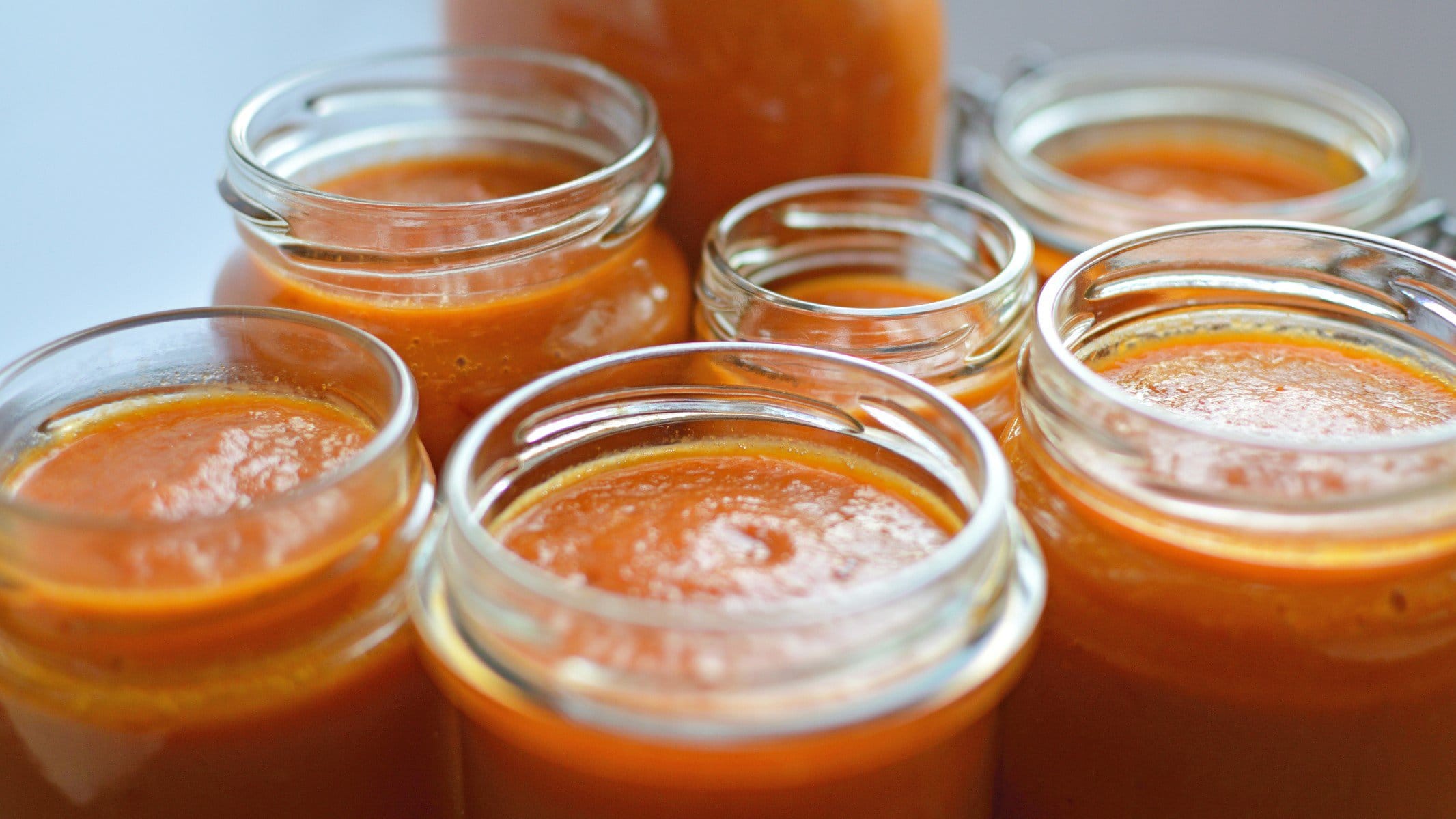 Orange-hellrote Habanero Hot Sauce in verschieden großen offen Einmachgläsern aus der Frontalsicht.