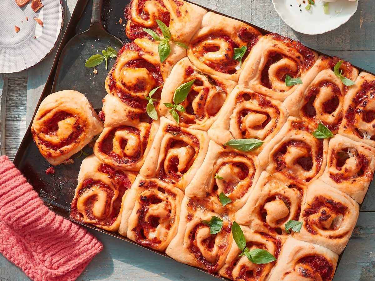 Auf einem Backblech liegen eingerollte Pizzaschnecken mit Tomatensauce und Käse.