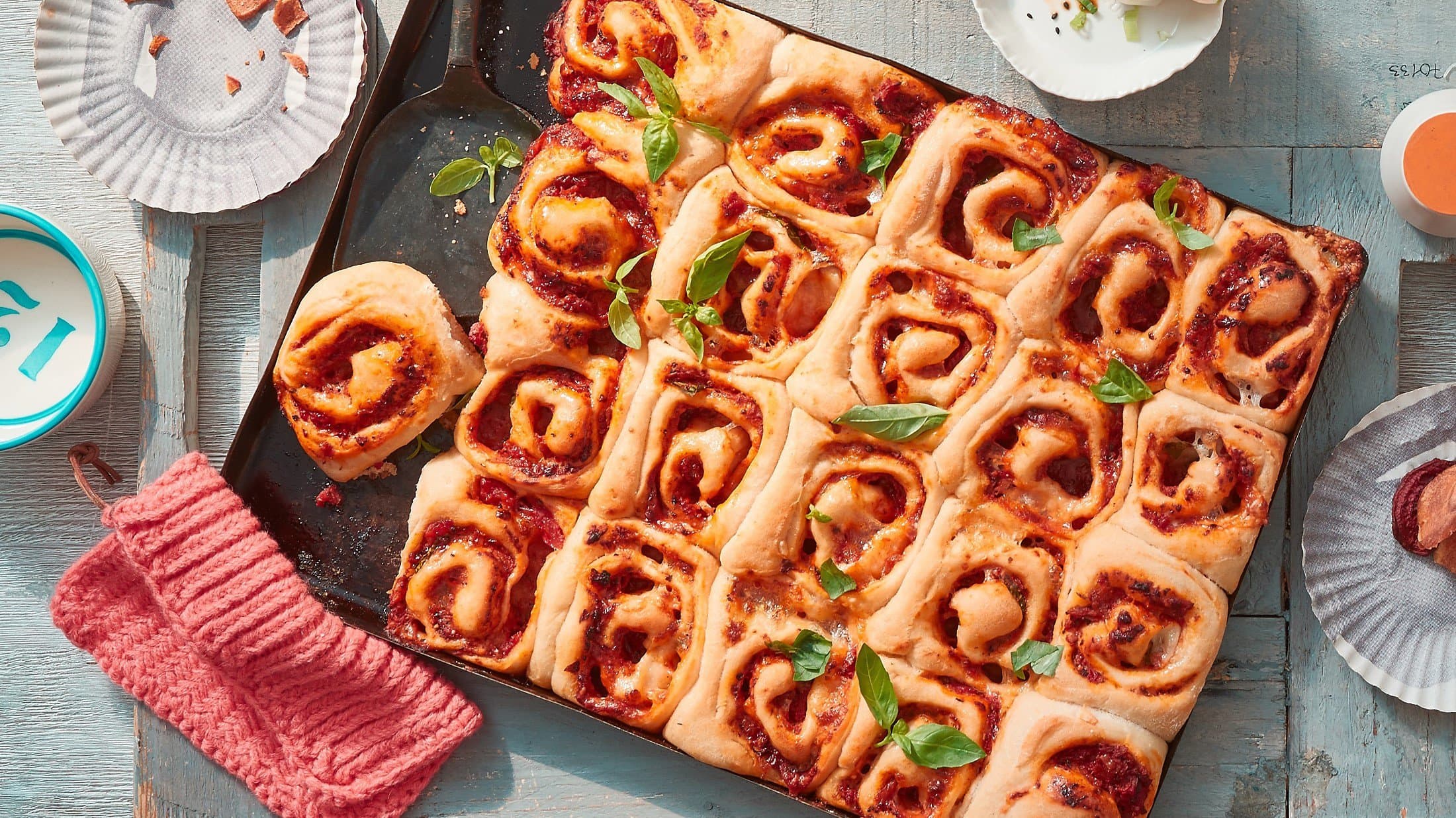 Auf einem Backblech liegen eingerollte Pizzaschnecken mit Tomatensauce und Käse.