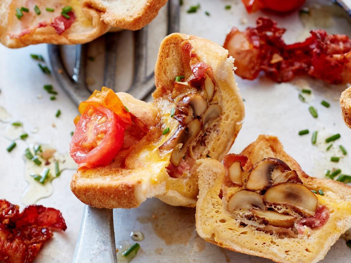 Auf einem Blech liegen aufgeschnittene Toast-Muffins gefüllt mit Tomaten und Champignons.