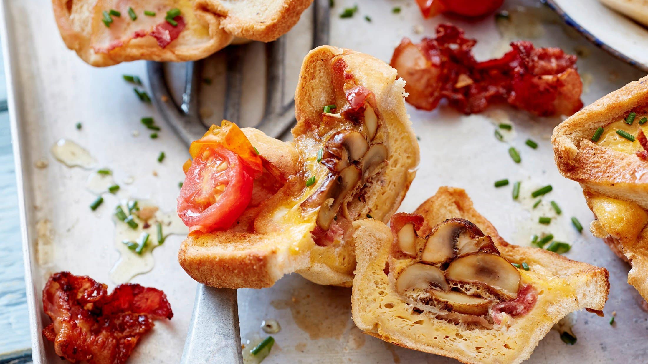 Auf einem Blech liegen aufgeschnittene Toast-Muffins gefüllt mit Tomaten und Champignons.